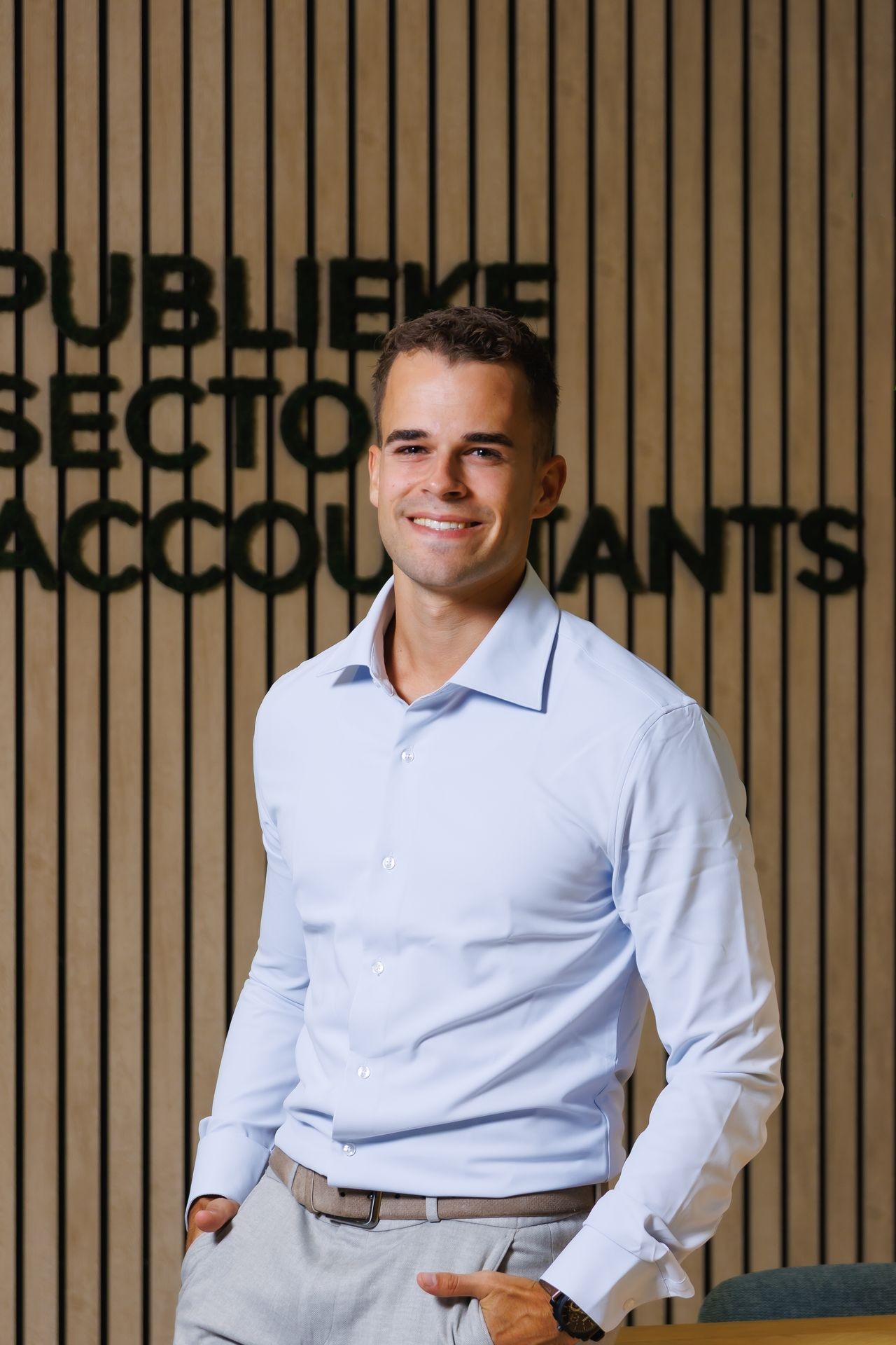 Medewerker van Publieke Sector Accountants poseert voor de PSA-achterwand in een professionele kantoorsetting.