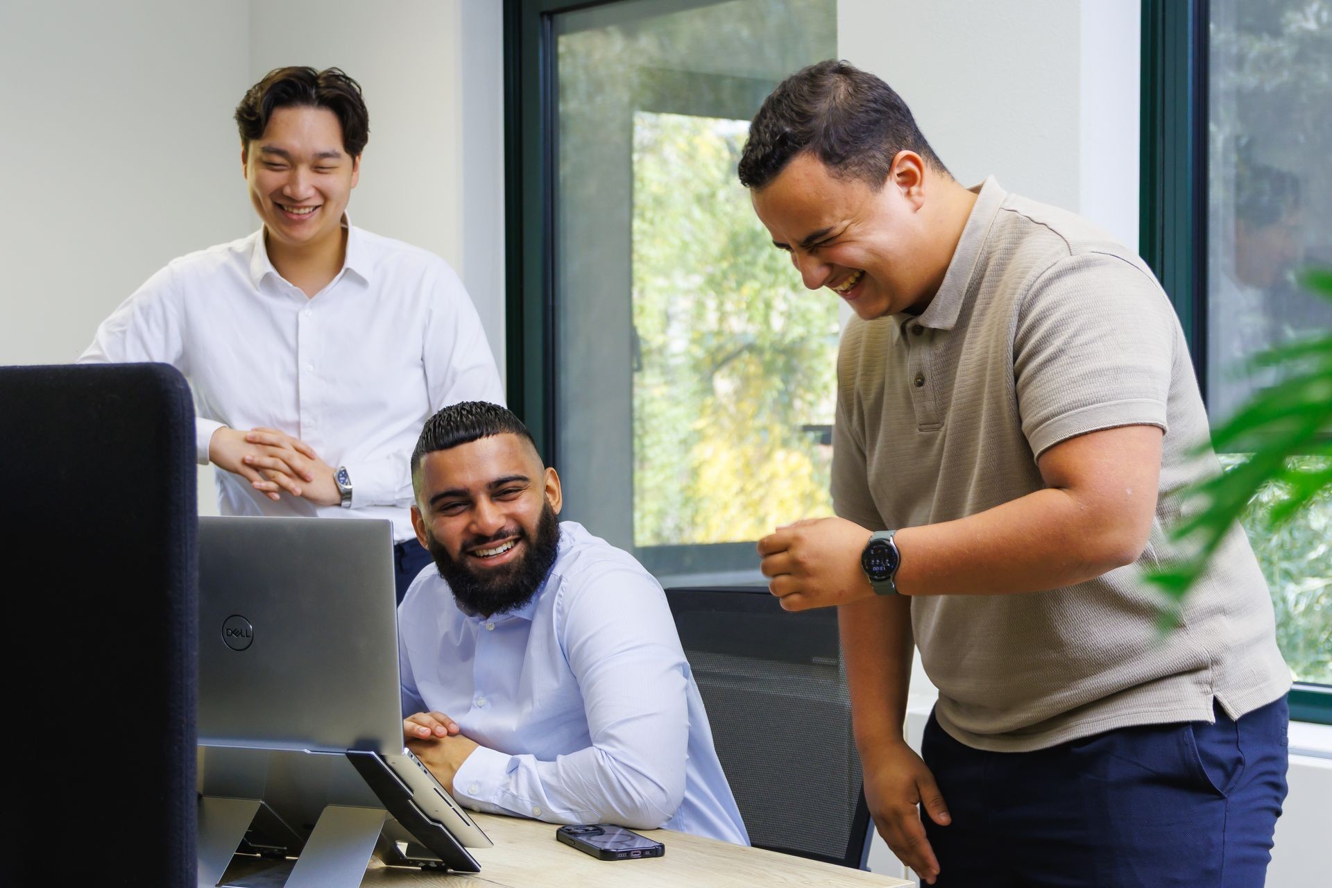 Drie collega’s die samenwerken achter een laptop in een kantooromgeving.