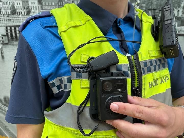 Handhaver met bodycam en portofoon op veiligheidsuniform.