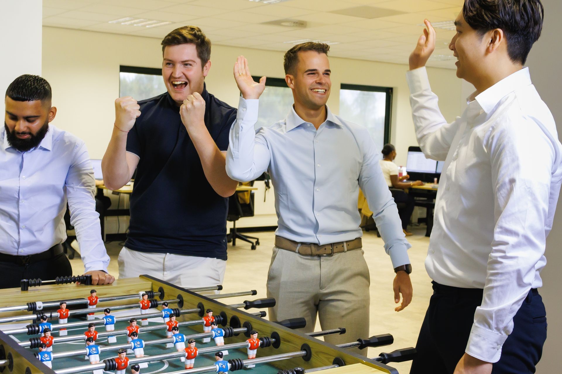 Collega’s van Publieke Sector Accountants die samen plezier hebben bij de tafelvoetbaltafel in een informele kantooromgeving.