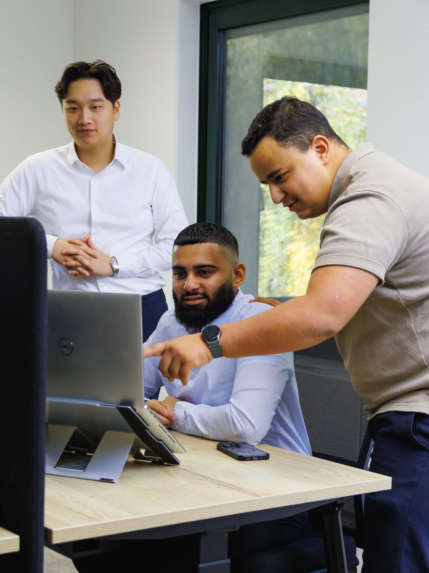 Drie collega’s die samenwerken achter een laptop in een kantooromgeving.