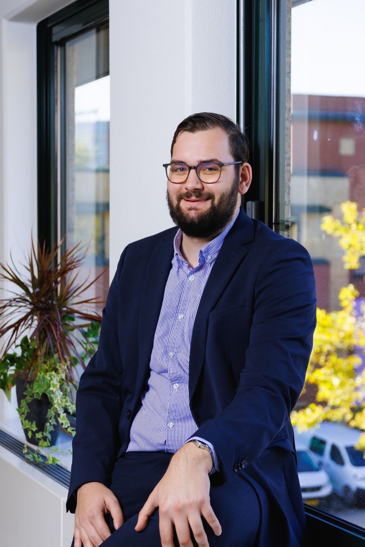 Collega in zakelijke outfit die poseert bij het raam in de kantoorruimte van Publieke Sector Accountants.