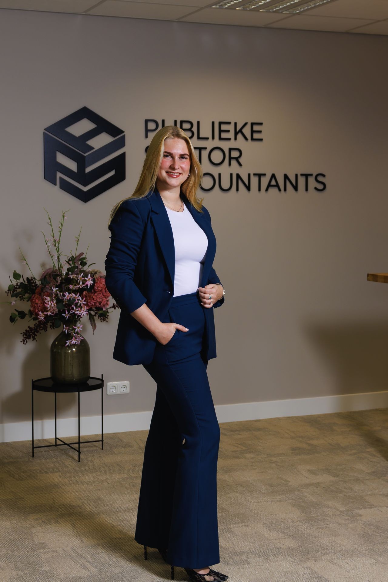 Collega van Publieke Sector Accountants poserend in de entree van het kantoor voor het bedrijfslogo.